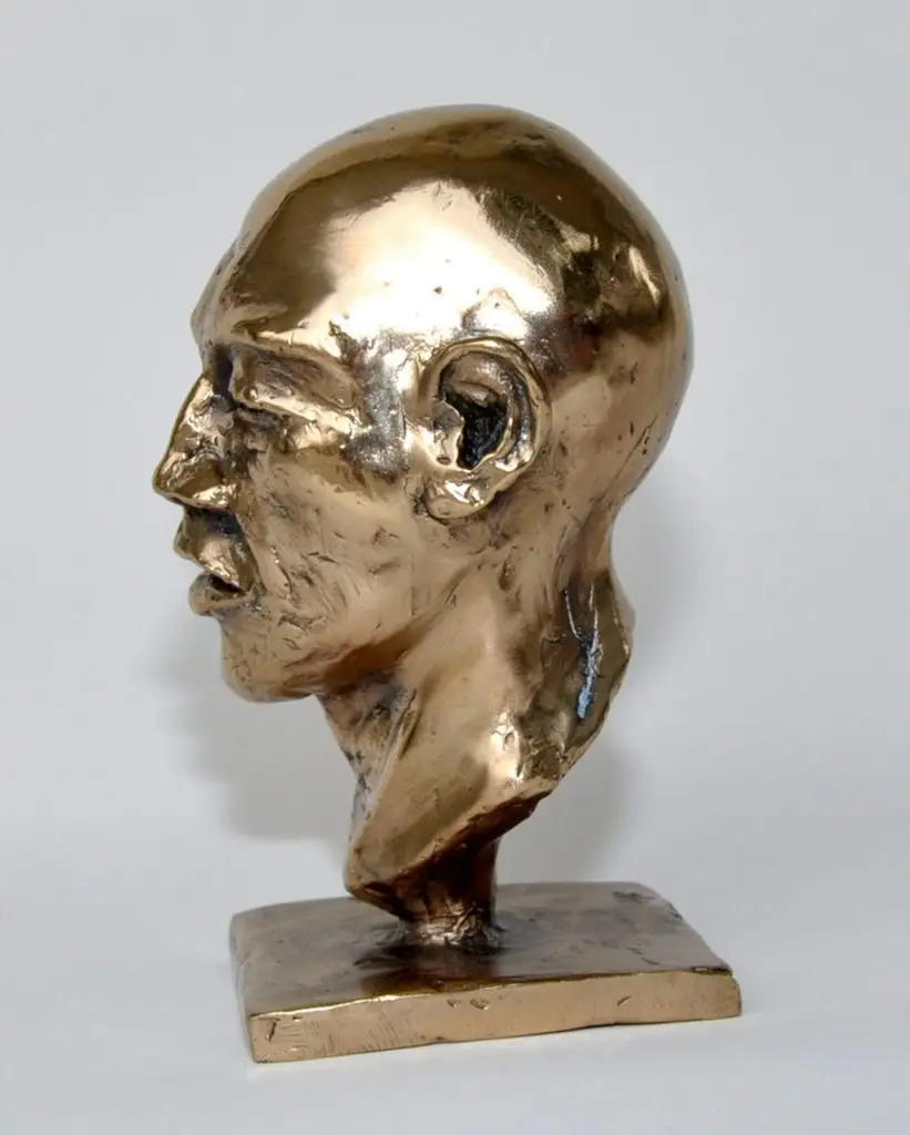 A bronze sculpture of the left-side profile of a bald man head