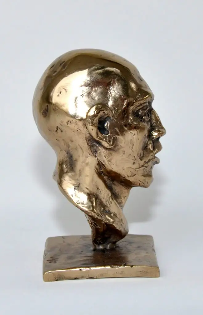 A bronze sculpture of the right-side profile of a bald man head